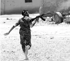  ?? — Reuters photo ?? A Kurdish fighter from the People’s Protection Units (YPG) fires his rifle at Islamic State militants as he runs across a street in Raqa.