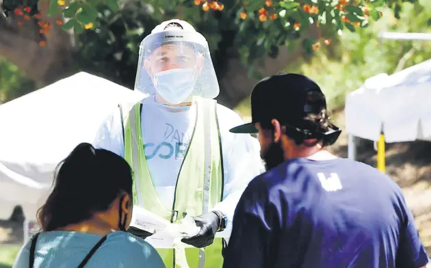  ??  ?? A volunteer dressed in full protective equipment offers test kits to people at a walk-in COVID-19 test site in Los Angeles, California, U.S., June 30, 2020.