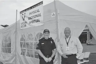  ?? Staff photo by Neil Abeles ?? Nelson Gagne, right, is shown with Atlanta police Officer David Rumsey before the large yellow tent at the Atlanta Forest Festival. Gagne is trying to distribute informatio­n about the county’s Victim Relief Ministries.