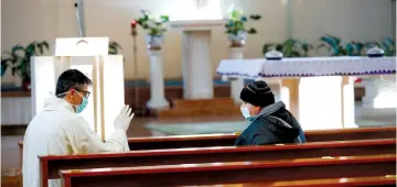  ?? (Reuters/Remo Casilli) ?? A PRIEST wearing a mask and protective gloves listens to a confession by a member of his congregati­on while practicing social distancing at the S.S. Sacramento church in Rome yesterday.