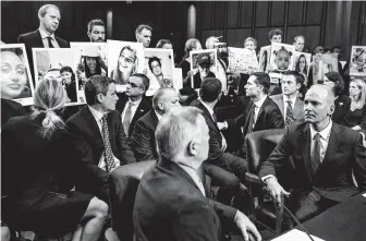  ?? Andrew Harnik / Associated Press ?? Boeing CEO Dennis Muilenburg, right, watches during a Senate hearing Tuesday as family members hold up photograph­s of those killed after two Boeing 737 Max jets crashed in the past year.