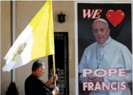  ?? FOTO: HADI MIZBAN / AP / NTB ?? En prest holder et vatikansk flagg mens han går forbi en plakat med bilde av Pave Frans i Bagdad. Irak får fredag sitt første pavebesøk.