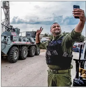  ?? AP/BADERKHAN AHMAD ?? A member of the Kurdish Asayish, or Internal Security Forces, gets a selfie with a Russian military vehicle in the background Friday near the border with Turkey in northern Syria. Russian forces are patrolling the region as part of a deal with Turkey.