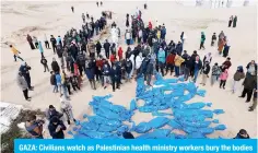  ?? — AFP ?? GAZA: Civilians watch as Palestinia­n health ministry workers bury the bodies VM \UPKLU[PÄLK 7HSLZ[PUPHUZ HM[LY [OL` ^LYL YL[\YULK I` [OL APVUPZ[ LU[P[` PU H mass grave east of Rafah in the southern Gaza Strip on Jan 30, 2024.