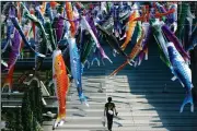  ?? (AP/Eugene Hoshiko) ?? A man walks under carp-themed streamers fluttering Saturday in Tokyo. The streamers were hung to mark Children’s Day on Tuesday, wishing the kids healthy growth like carp that can swim up waterfalls.
