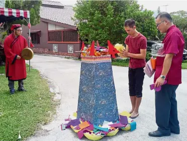  ??  ?? Doing it right: The traditiona­l ‘deu lao’ ceremony culminated in Mook (centre) burning a flower tower and other paper parapherna­lia while Taoist priests Tham Wai Yin (right) and Wai Leong continue the recital.