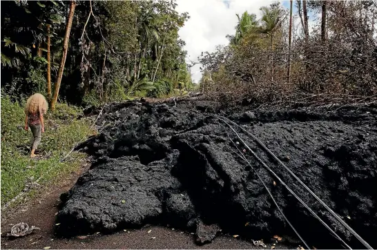  ?? AP ?? Leilani Estates resident Hannique Ruder walks past a mound of hardened lava released by the Kilauea volcano, which has covered a street in the subdivisio­n. Kilauea has been spewing lava for over a week, and scientists are now warning of the possibilit­y of a violent eruption caused by trapped steam.