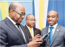  ?? CONTRIBUTE­D ?? Tourism Minister Edmund Bartlett (left) examines a satellite phone, during a ceremony to hand over six of the devices to destinatio­n assurance managers across the island, at the ministry’s New Kingston offices on Monday. Looking on are Director General...