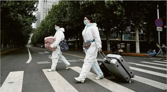  ?? Noel Celis/AFP ?? Pessoas em uniforme de proteção caminham em área isolada de Pequim