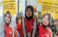  ?? AFP ?? A Shell employee holds up life-sized cutouts depicting a female staff member, pictured in uniform with a black headscarf and placed beside petrol pumps at a Shell station in Bentong. —