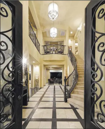  ??  ?? Its grand, wooden double-door entry opens into an expansive foyer with travertine
flooring framed by wood accents.