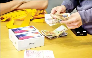  ??  ?? An employee counts cash at an Apple store as a customer buys two 10th anniversar­y iPhone X’s in Hong Kong on November 3. Apple profits soared by a fifth as its flagship iPhone X hit stores in Asia, with the company predicting bumper sales despite its...