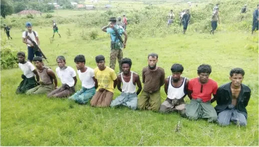  ??  ?? TEN ROHINGYA MUSLIM men with their hands bound kneel, as members of the Myanmar security forces stand guard in Inn Din village, September 2, 2017.