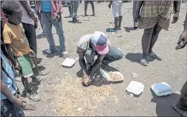  ??  ?? A man picks up food that was accidently spilled on the ground in Les Cayes, Haiti.