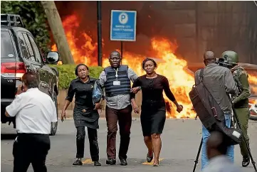  ?? AP ?? Security forces help civilians flee the attack on a hotel complex in Nairobi as cars burn behind them. Somalia-based extremist group al Shabaab has claimed responsibi­lity.