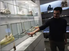  ?? (AP) ?? A store manager points out Yeezy shoes made by Adidas that were displayed inside cases at Addict shoe store in Brickell City Center in Miami in October.