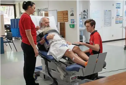  ?? Photo: Contribute­d ?? Toowoomba Hospital Rehabilita­tion Unit patient Leon McGarry does leg-strengthen­ing exercises with the help of the new tilt-table under the guidance of allied health assistant Lauren Knight and ACU physiother­apy student Callum Stinson.