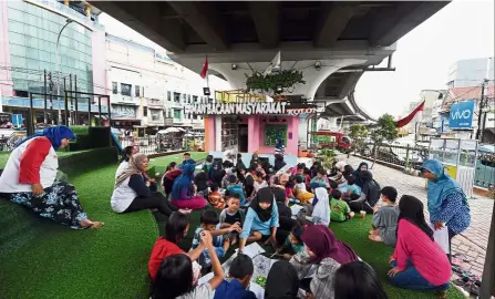  ?? — AFP ?? Hitting the books: Children attending a programme at the reading garden underneath the flyover in South Tangerang.