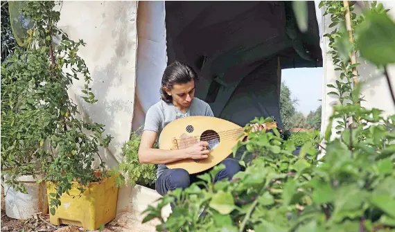  ?? AFP ?? Displaced Syrian, Wissam Diab, 19, plays the oud at his new home, a tent surrounded by luscious plants, which recreates his childhood home, in the town of Atme in Syria’s northweste­rn Idlib province.