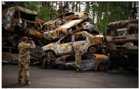  ?? (AP/Emilio Morenatti) ?? A Ukrainian territoria­l defense force fighter poses Saturday next to a pile cars destroyed during the Russian occupation in Irpin, on the outskirts of Kyiv.