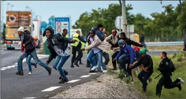  ??  ?? Making their move: Police chase migrants as they run towards lorries queueing at Calais