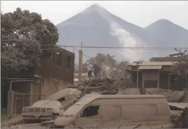  ?? The Associated Press ?? Rescue workers walk on rooftops in Escuintla, Guatemala, on Monday, blanketed with heavy ash spewed by the Volcan de Fuego — or “Volcano of Fire” — pictured in the background. A fiery volcanic eruption in south-central Guatemala sent lava flowing into...