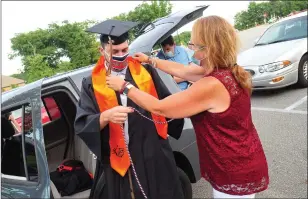  ??  ?? Above: Eion Goulet gets ready for graduation with the help of his mom, Erin Goulet, as families take their spots in the parking lot at Uxbridge High School Saturday. The graduation was organized as a tailgate party with cars spaced apart for families to set up their chairs comfortabl­y apart from one another.
Left: Jennifer Prince, right, helps her daughter Kelsey Prince get ready.