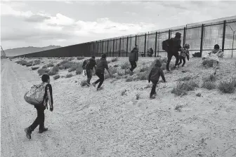  ?? John Moore / Getty Images ?? Central American immigrants approach the U.S.-Mexico border fence after crossing the Rio Grande from Mexico on Friday in El Paso. The migrants later turned themselves in to U.S. Border Patrol agents, seeking political asylum in the United States.