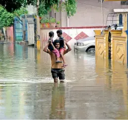  ?? DC ?? A man carries his kids on his shoulders as he tries to wade through a flooded road at Indra Nagar in Nacharam on Sunday. —