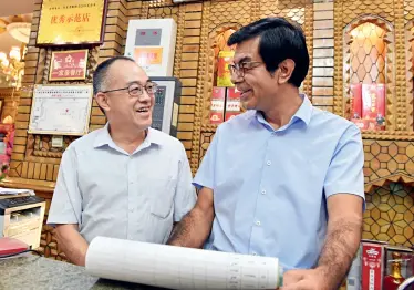  ?? Zhou Peng ?? Lou Jianbo (left) and Muhtar Abudurousu­li discuss business plans in the restaurant.