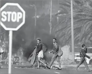  ?? PICTURE: EPA/AFRICAN NEWS AGENCY (ANA) ?? Pupils on their way home from school walk past a burning barricade during protests against evictions in Ocean View. Several families were evicted because of alleged illegal occupation of land, sparking the community to protest. Housing and the lack...