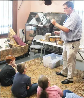  ?? Brodie Johnson • Times-Herald ?? At the St. Francis County Museum’s Summer Enrichment classes, children learn many different things about history, including blues music. Richard Spilmon, with the Delta Cultural Center, talks to children about early instrument­s used in creating music. Spilmon holds a cowbell to demonstrat­e how it was used in music. The summer enrichment classes are held at the museum on Tuesdays, from 11 a.m. until 1 p.m.