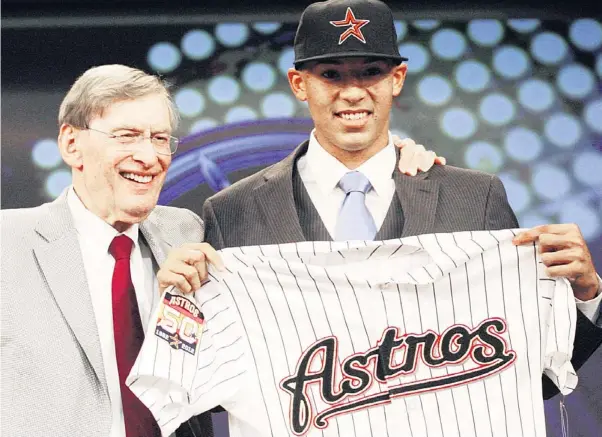  ??  ?? CARLOS CORREA exhibe orgulloso su nueva camiseta de los Astros de Houston luego de ser reclamado en el primer turno. A su izquierda, el comisionad­o Bud Selig.