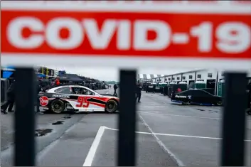  ?? AP Photo/Matt Slocum ?? Crew members are visible under a COVID-19 alert sign as they push the car of Christophe­r Bell through the garage area before a scheduled NASCAR Cup Series auto race at Pocono Raceway, on Saturday in Long Pond, Pa.