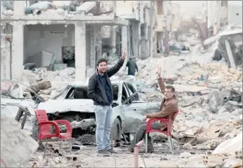  ??  ?? Men raise the peace sign amid devastatin­g scenes of destructio­n in their home town, Kobane, Syria.