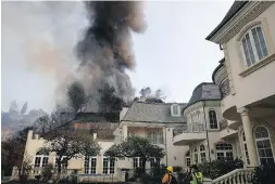  ??  ?? Smoke rises from flames working their way down a slope behind a mansion in the Bel-Air district of Los Angeles on Wednesday.