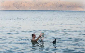  ??  ?? A MAN READS a newspaper in the Dead Sea.