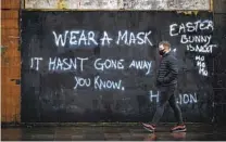  ?? LIAM MCBURNEY AP ?? A man wearing a face covering walks past graffiti on the Lower Newtownard­s Road in Belfast on Friday.