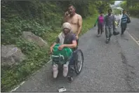  ?? The Associated Press ?? RISKY MIGRATION: Honduran migrant Omar Orella pushes fellow migrant Nery Maldonado Tejeda in a wheelchair, as they travel with hundreds of other Honduran migrants making their way the U.S., near Chiquimula, Guatemala on Tuesday. Maldonado said he lost his legs in 2015 while riding “The Beast,” a northern-bound cargo train in Mexico, and that this is his second attempt to reach the U.S.