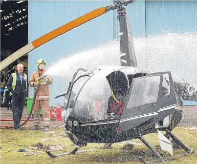  ?? Pictures: Mhairi Edwards. ?? A firefighte­r douses down the helicopter following the crash.