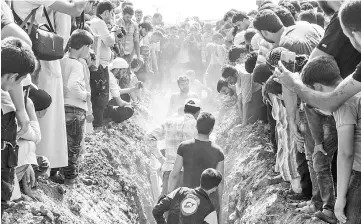  ??  ?? Members of the White Helmets bury their fellow comrades during a funeral in Sarmin. — AFP photo