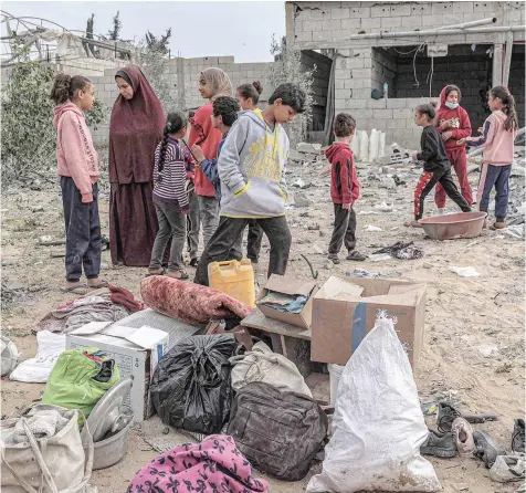  ?? — AFP ?? Women and children stand by items that were salvaged from a building that was hit overnight during Israeli bombardmen­t in Rafah.