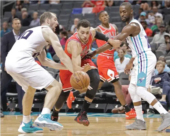  ?? CHUCK BURTON/AP ?? Bulls guard Zach LaVine (attempting to drive between the Hornets’ Cody Zeller and Kemba Walker) scored a game-high 26 points in preseason action Monday.