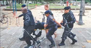  ??  ?? Traficante­s descem armados a pedra da Praia Vermelha (esquerda). Um dos homens segura um fuzil. Policiais militares carregam um colega ferido por estilhaços de granada na Praia Vermelha (direita)