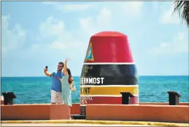  ?? ROB O’NEAL — THE KEY WEST CITIZEN VIA AP ?? Left, Key Westers James Sandlin, left, and Chloe Hodgdon, take advantage of a deserted “Southernmo­st Point of the United States” to take a photo Thursday while waving to relatives via a nearby webcam in Key West. The location is usually packed with...