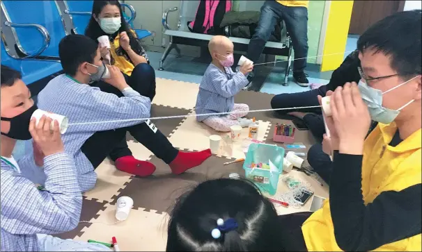  ?? YUAN QUAN / XINHUA ?? Volunteers help children to use “telephones” made from paper cups and string to explain how sound waves move.