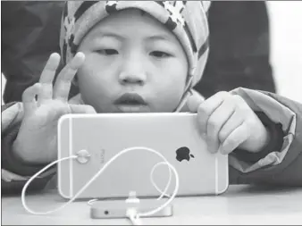 ?? HUANG JIEXIAN / FOR CHINA DAILY ?? A boy plays with a smartphone in an outlet of Apple Inc in Qingdao, Shandong province.