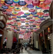  ?? — AFP ?? People walk under a passage ( extreme left) covered with umbrellas at the Dubai Mall in the Gulf emirate of Dubai, workers ( centre) working outside the Raj Mahal area, which is part of the Bollywood park of Dubai Parks and Resorts ( DPR), and a...