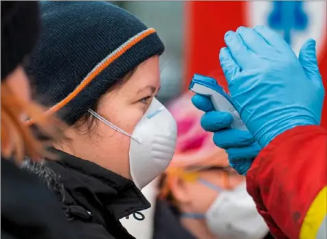  ?? Joe Klamar/AFP via Getty Images ?? A Slovak firefighte­r checks the temperatur­e of a woman wearing a protective facemask Friday at the Bratislava-Jarovce border between Austria and Slovakia. The Slovak government has reintroduc­ed controls along its borders to prevent the new coronaviru­s from spreading further.