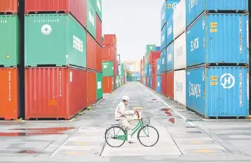  ??  ?? A worker rides a bicycle in a container area at a port in Tokyo. Japan logged a surplus in April of 615.7 billion yen (US$5.6 billion) with the US, up 4.7 per cent after a 0.3 per cent decline the previous month, as demand for cars and constructi­on...